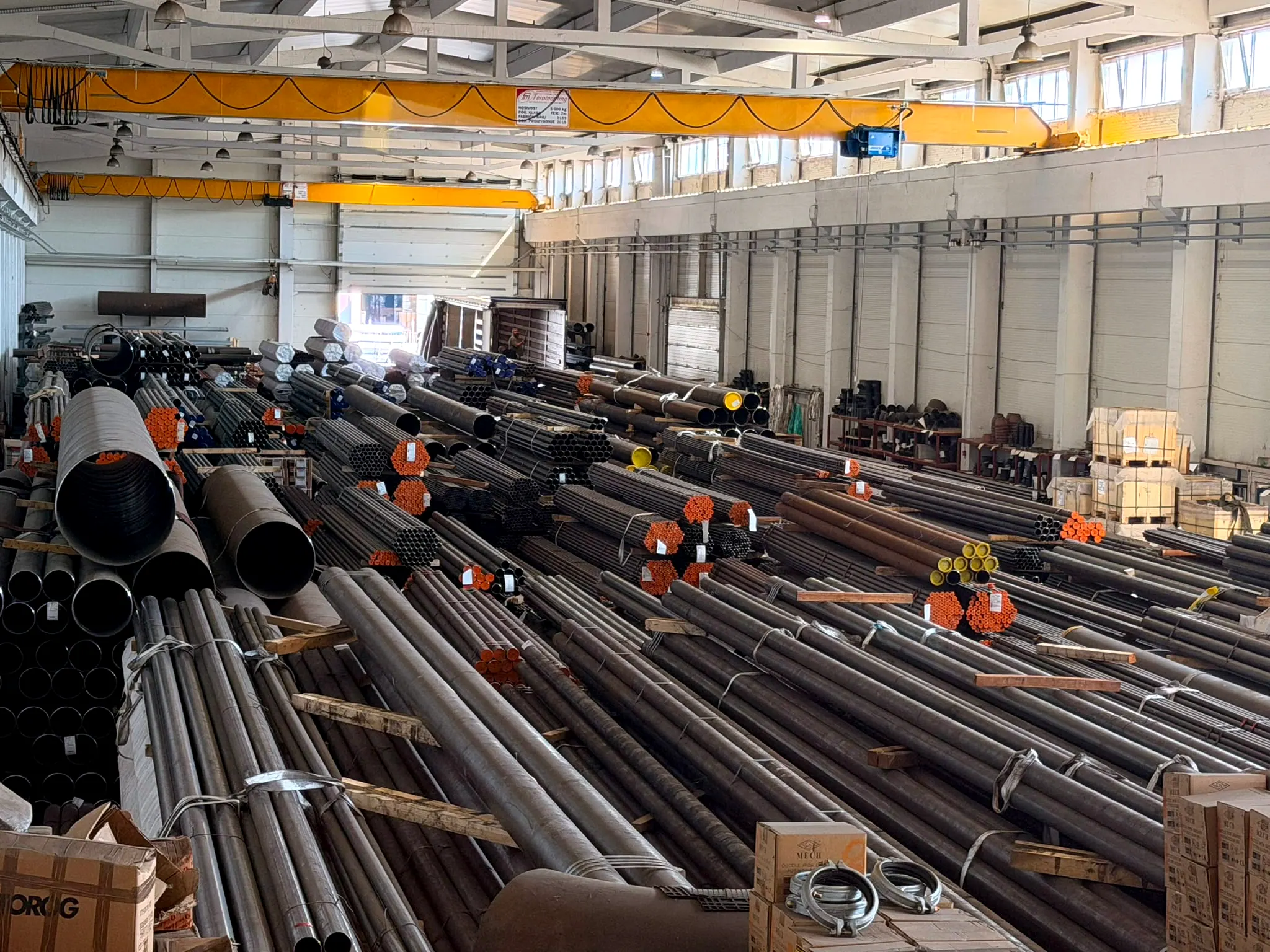 Interior of the PEZOS warehouse with an overhead crane and stacked steel pipes.
